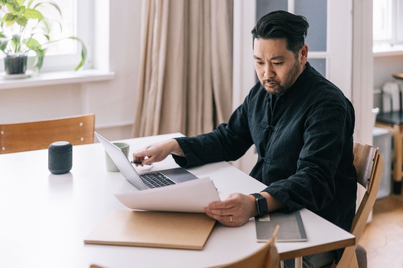 Man looking at paperwork and a laptop at a table