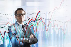 Person with glasses looking at the camera with a layer of stocks charts between the person and the camera.