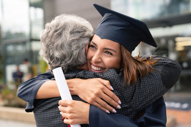 Young woman graduate smiling and hugging her mother, with diploma in hand