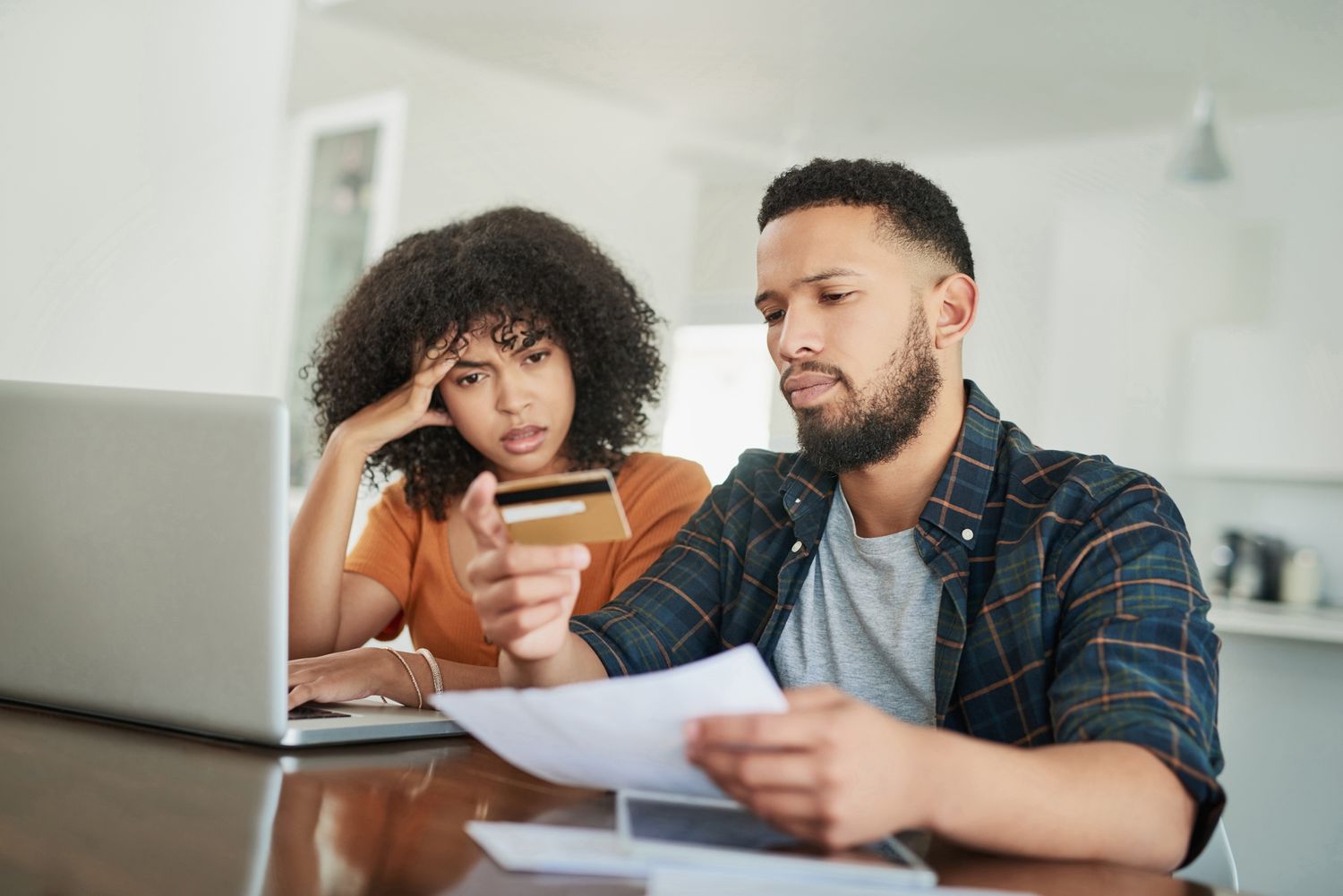 A man and woman sit at a table with a laptop, looking at a credit card.