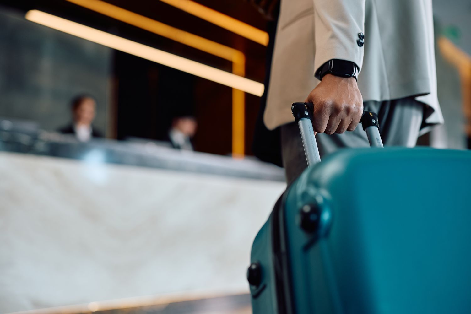 A close-up of a man with a suitcase approaching a hotel desk. 