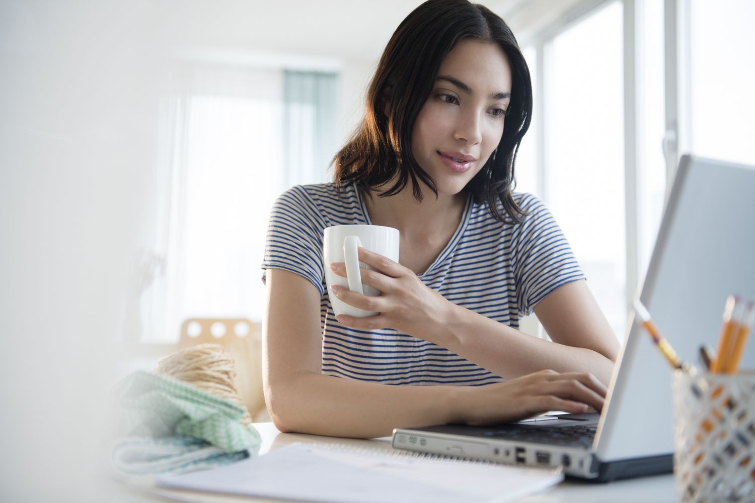 A woman sits at a desk with a coffee cup and a laptop