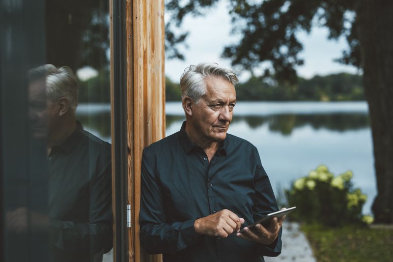 Senior man with tablet PC standing by glass wall at backyard