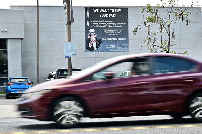 A car drives past a sign at an auto dealership selling used cars on April 28, 2025 in Alhambra, California.