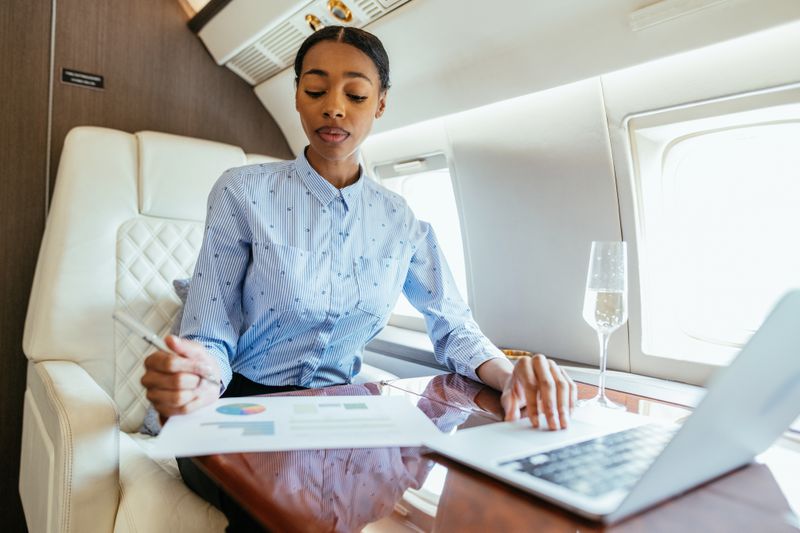 A woman working on a laptop and writing on a document while in a private jet