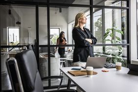 Satisfied looking business woman standing in a conference room and looking out the window.