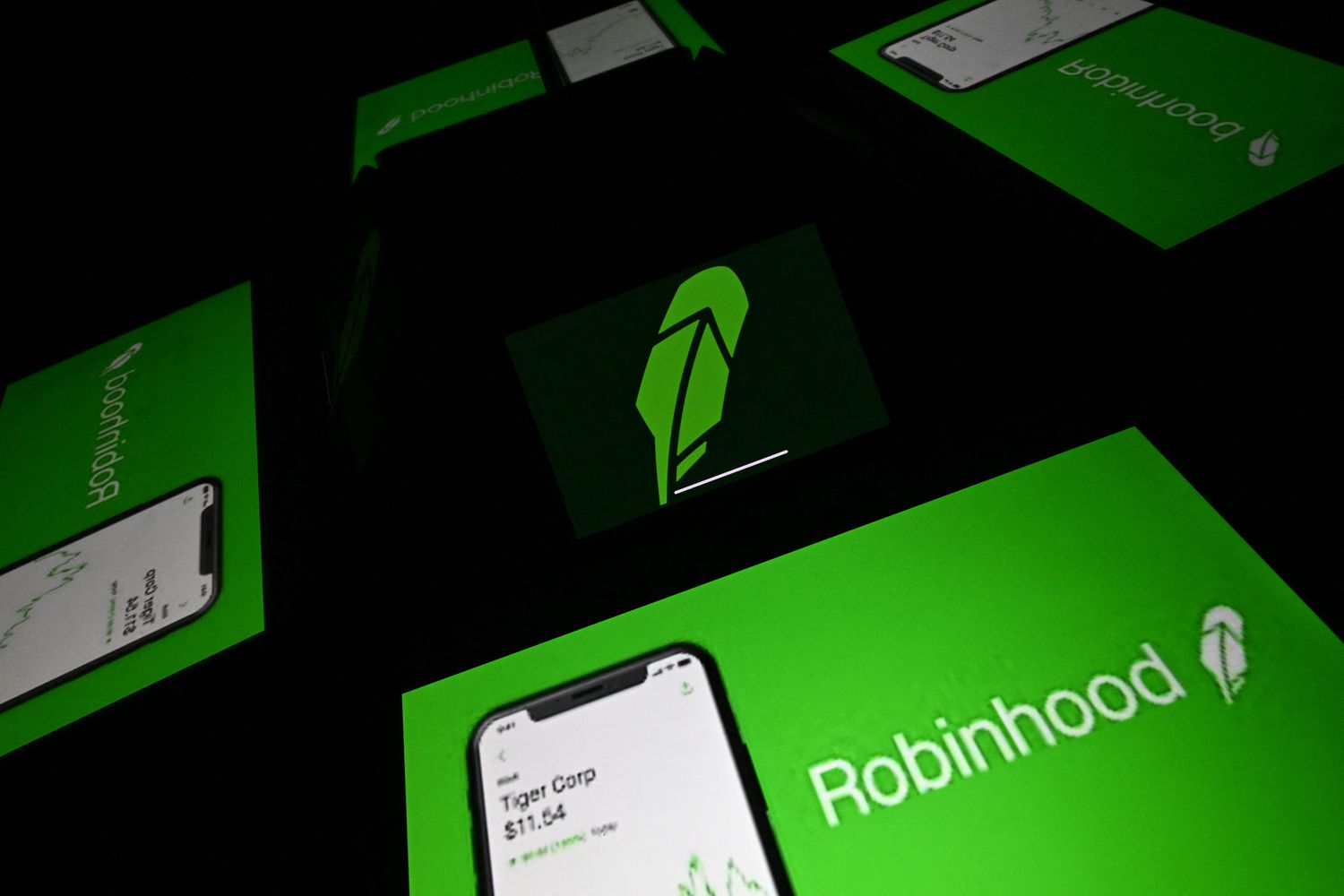 The Robinhood logo is seen in the center of four reflections of screens displaying the company's logo.