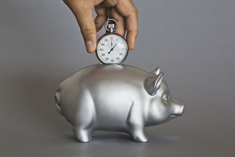 Hand holding pocket watch over silver piggy bank