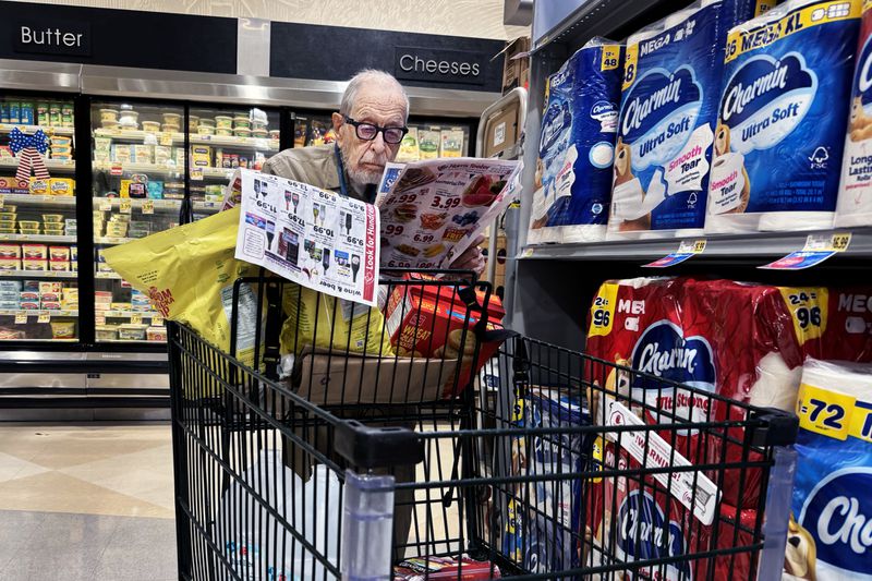 Person shopping in a grocery store, reading a flyer while leaning on a cart near the dairy aisle