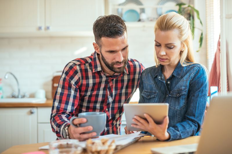Young couple sitting in their kitchen and looking together at bank rates on a tablet
