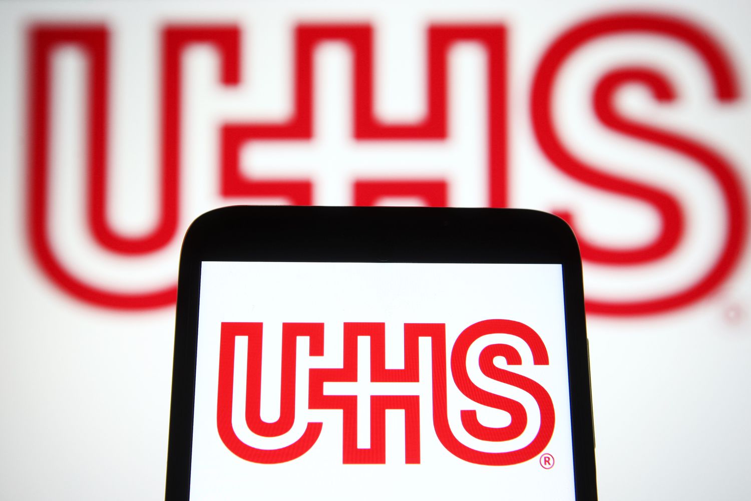 The red Universal Health Services logo is seen on a smartphone screen, with a larger version in the background.