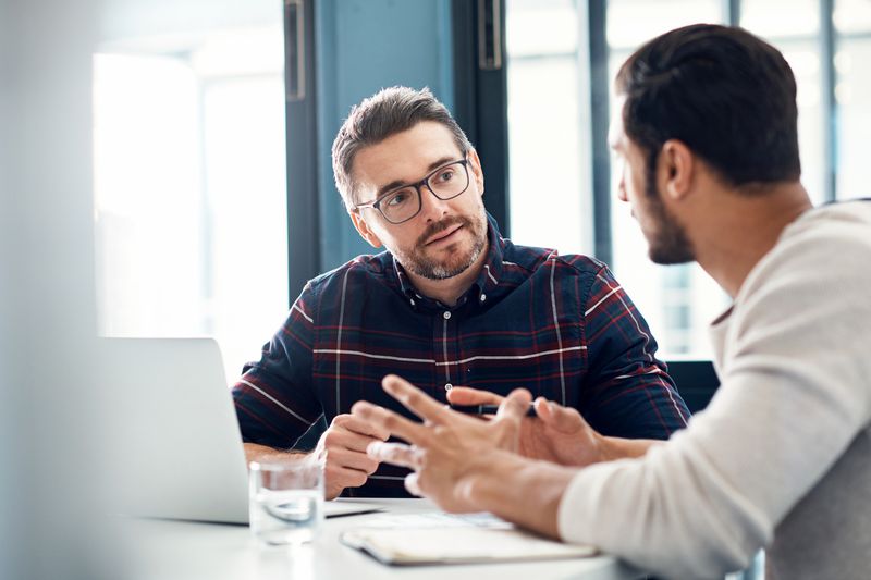 Two men have a discussion at a desk with documents about the best options to get $500 loan.