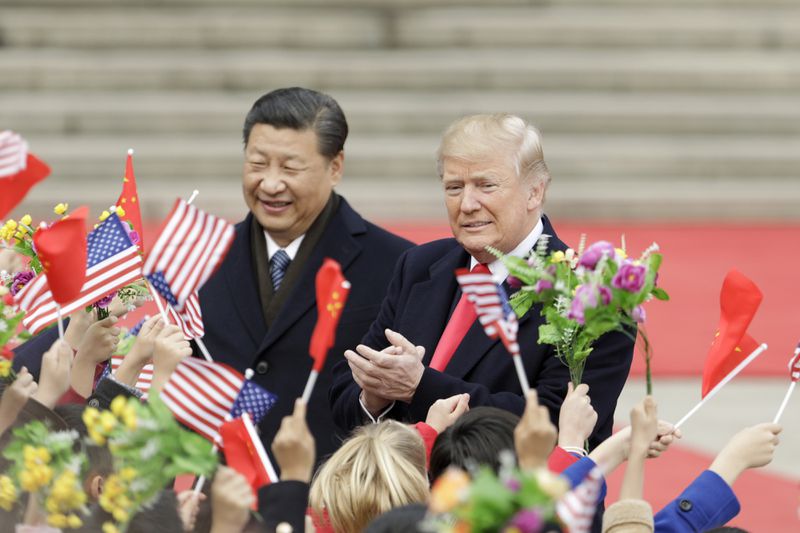 Xi Jinping and Donald Trump among a crowd holding flags and flowers, standing outdoors