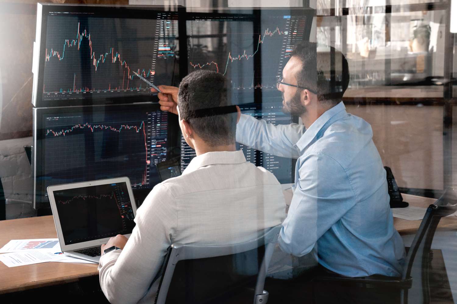 Two traders compare indexes on shown on computer screens in an attempt to predict market trends.
