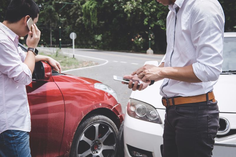 Men Using Mobile Phones By Broken Cars On City Street