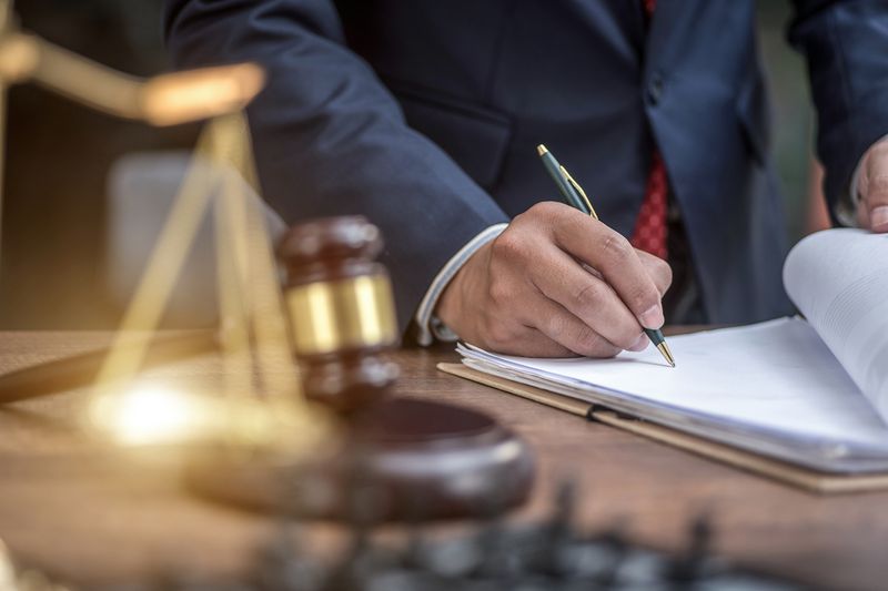 A person writes with a pen on a desk with a gavel on it.