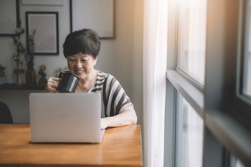 A woman works on a laptop and drinks coffee.