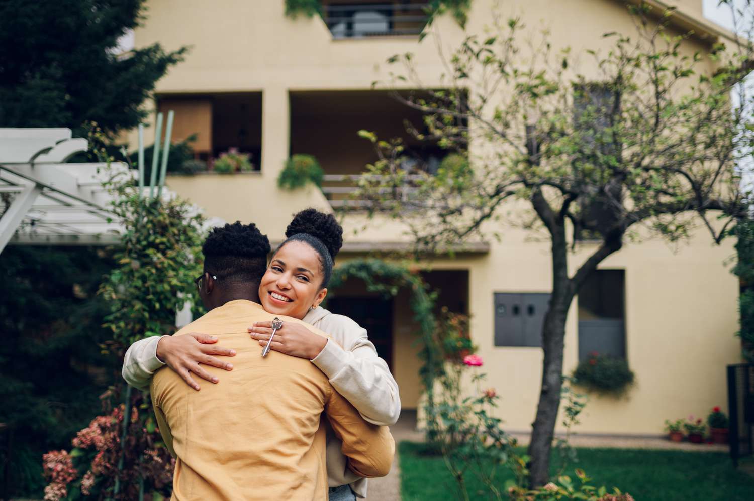 Multiracial couple hugging while standing in front of their new house, happy that they finally got approved for home insurance coverage.