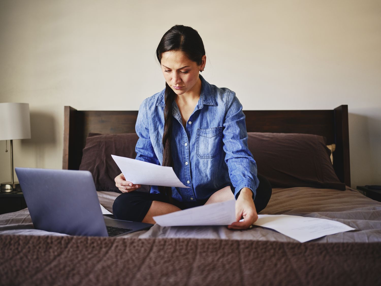 A woman sitting on her bed in a home working on a laptop.