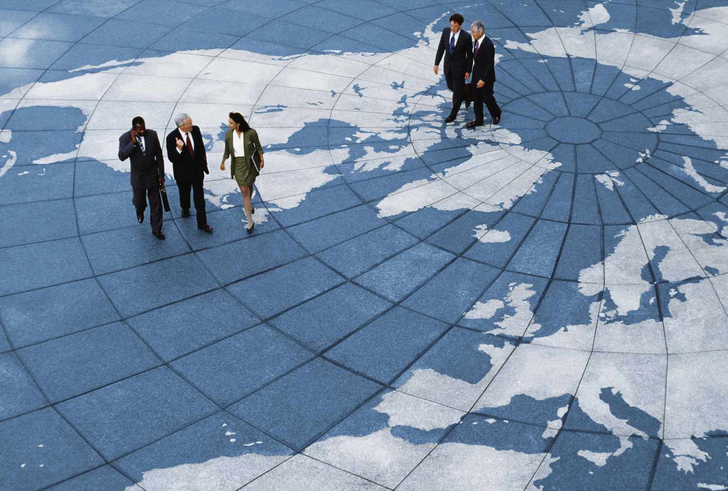 Groups of professionally dressed business people talk as they walk across an open plaza that is decorated to look like a globe.