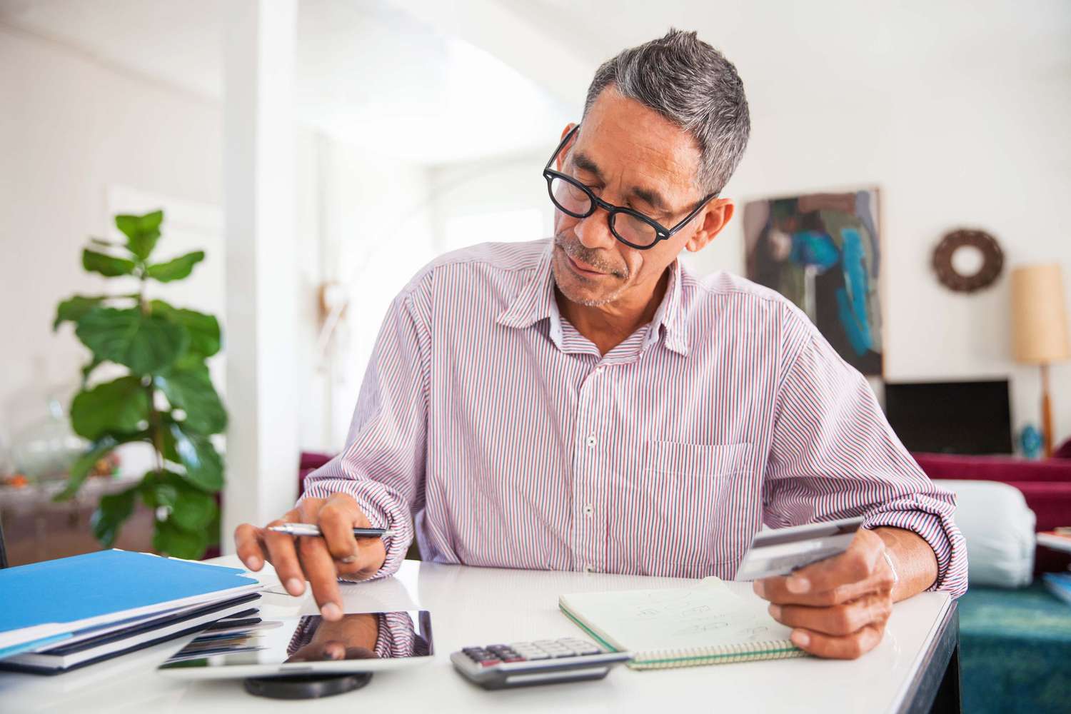 Mature man wearing eyeglasses at home using a credit card to make an online purchase