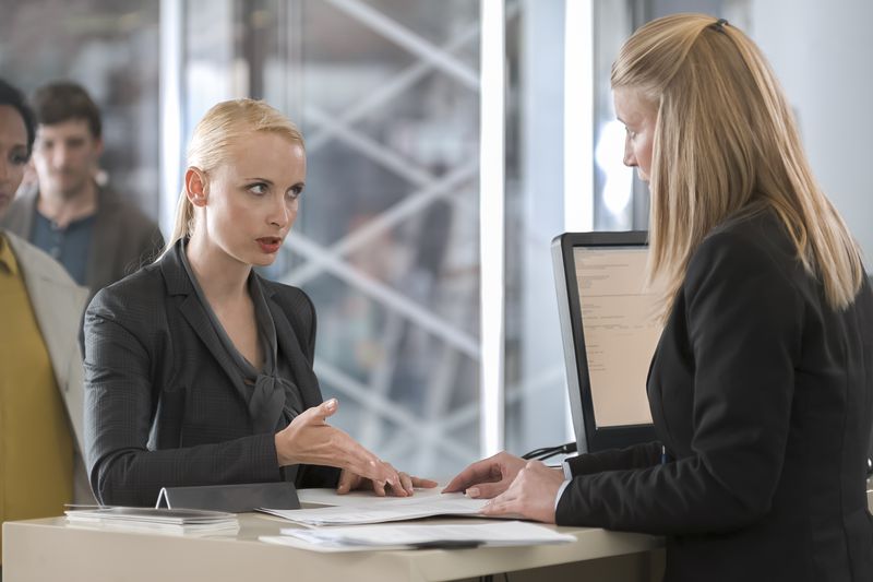 A woman speaking with a bank teller, others waiting in the background