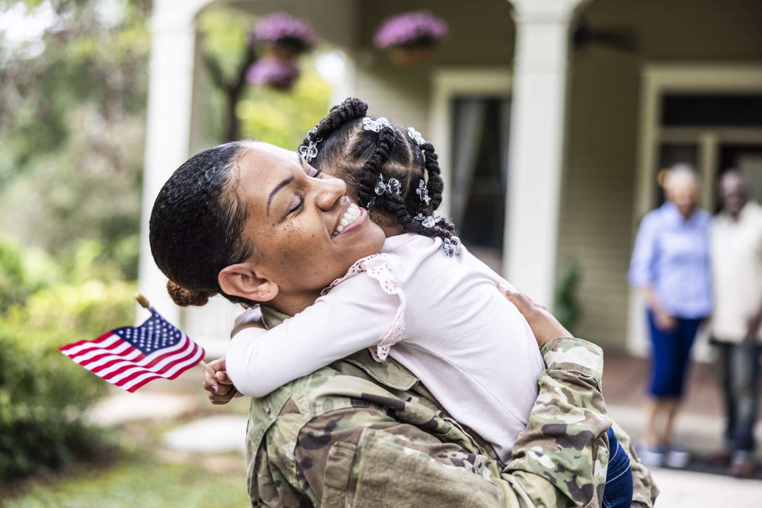 Daughter embracing U.S. soldier mother in front of their home.