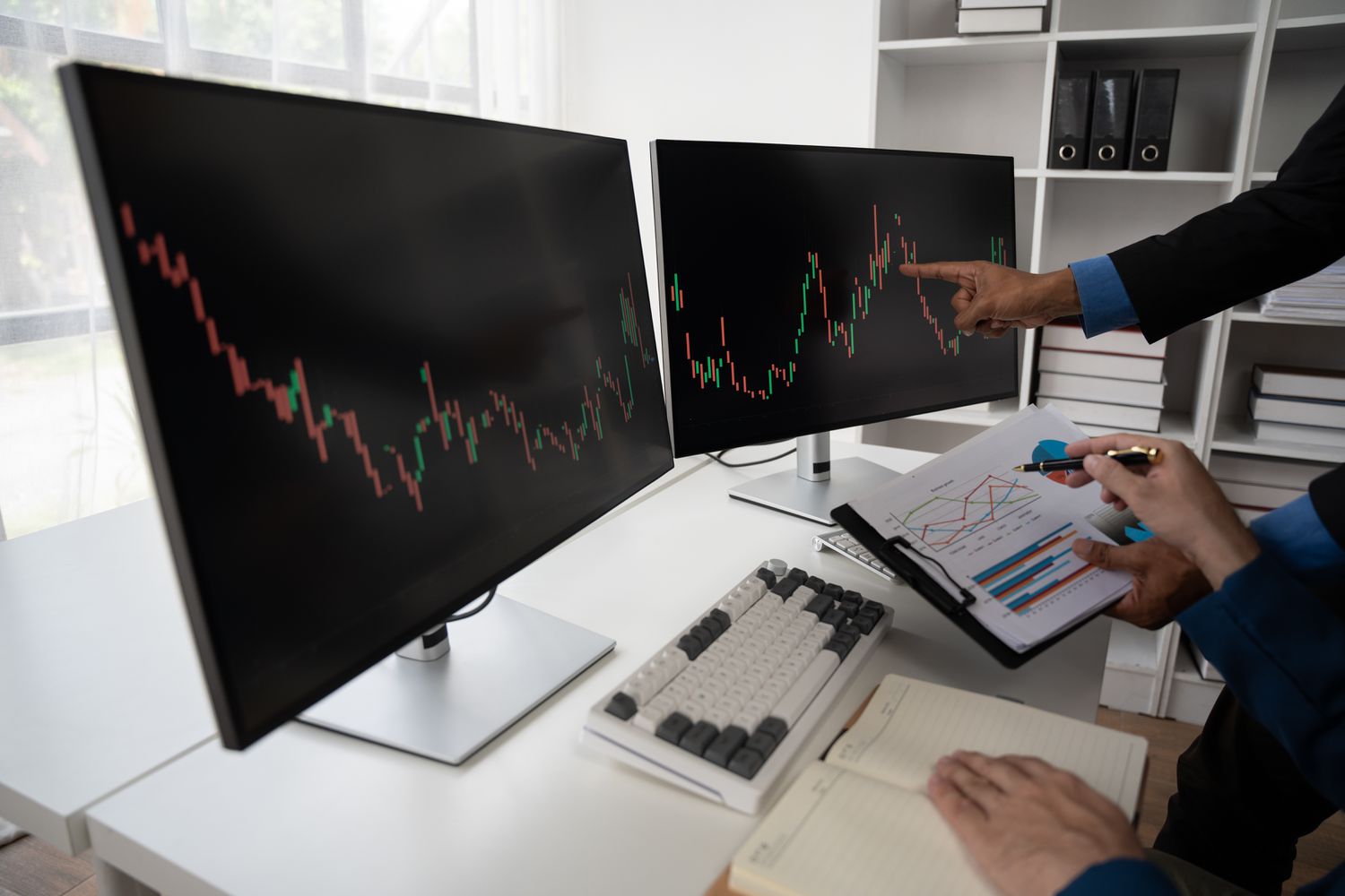 Hands pointing to detail on charts displayed on monitors