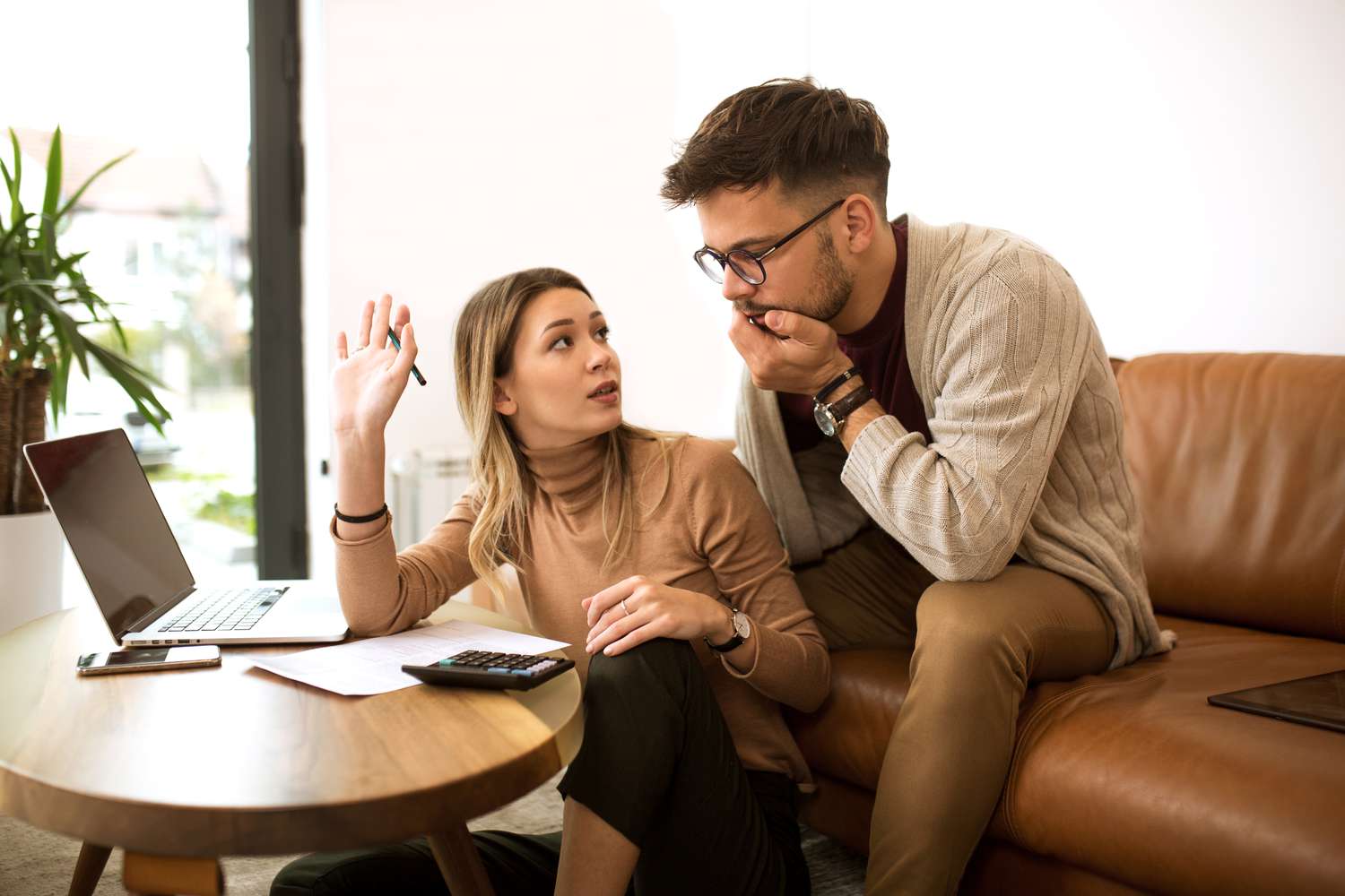 Young couple sitting on their sofa and looking with concern at documents and a calculator