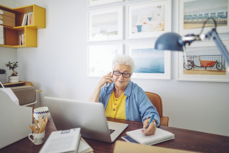 Woman working in an office while talking on a smart phone and taking notes.