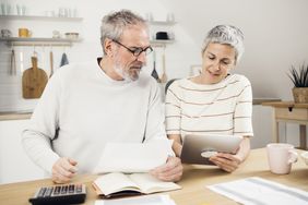 Older couple sitting in their kitchen and looking together at mortgage documents and rates on a tablet