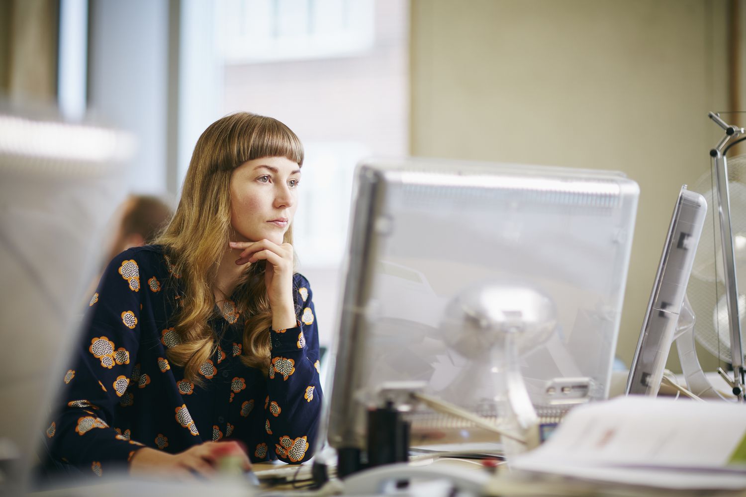 Young woman at a computer with two monitors in an office environment. 