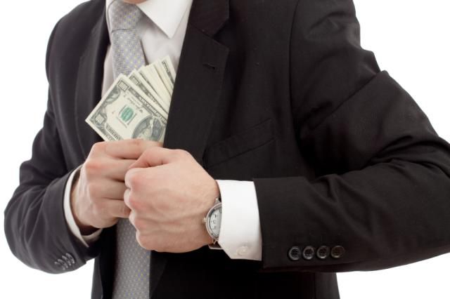 Man in suit with fancy watch stuffing wad of $100 bills into his inside jacket pocket