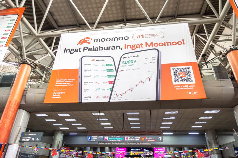 Image shows an advertisement banner for "moomoo," an investment platform, displayed at KL Sentral station Malaysia.