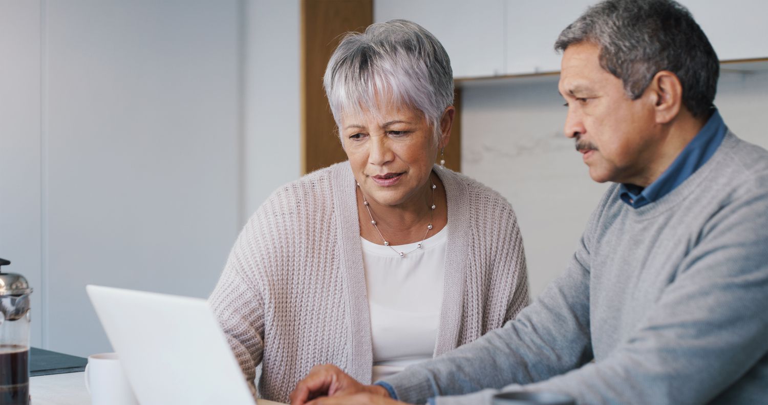 Older couple sitting at their kitchen counter and looking together at a laptop