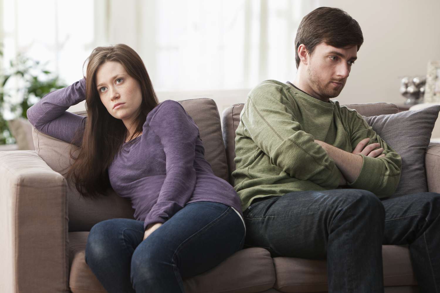 Couple angry at each other sitting on a couch next to each other but facing opposite directions