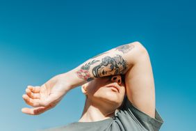 Woman covering her eyes with her arm with tattoo.