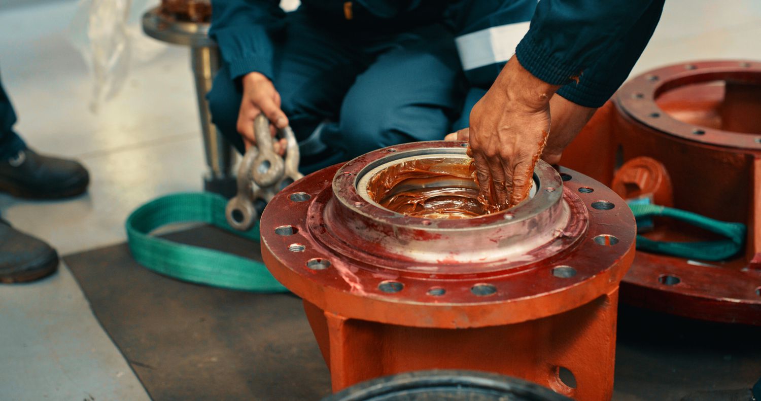 Male mechanics greasing a metal machine part in the workshop and fixing a mechanism for transmitting torque