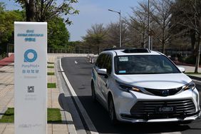 A white minivan robotaxi made by Pony AI drives by a sign that says PonyPilot