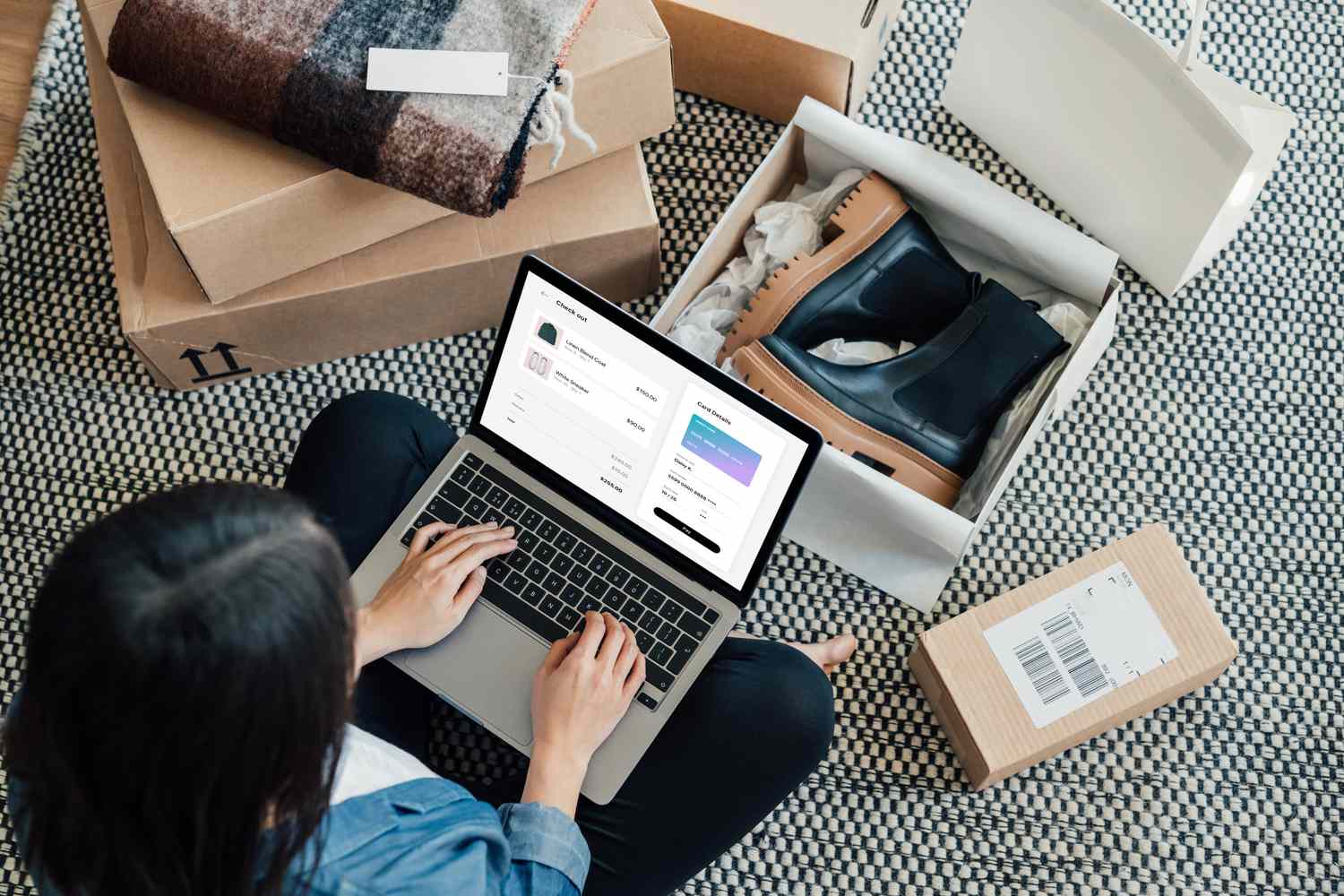 High-angle view of young woman on computer surrounded by packages, one of them open with a pair of boots inside