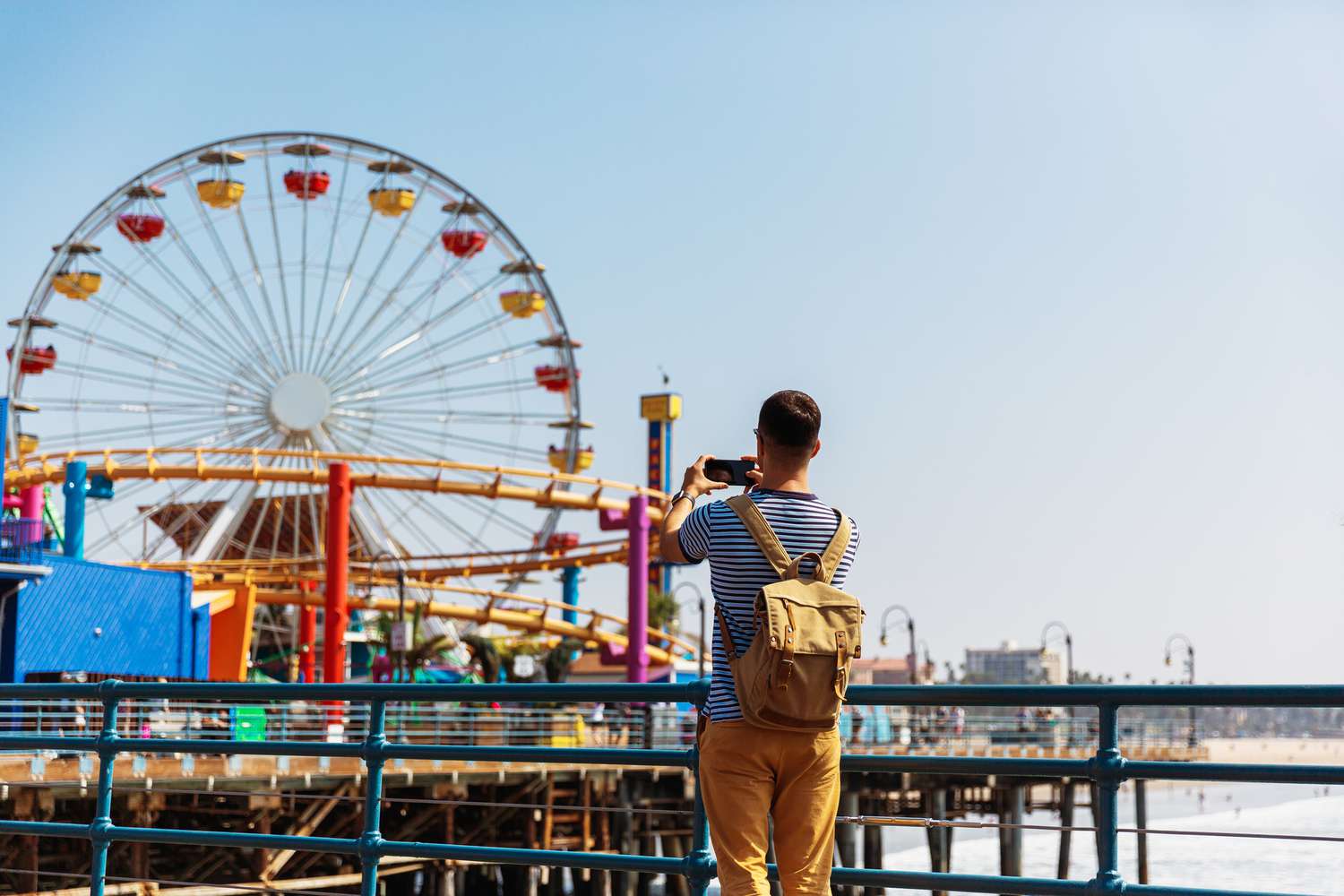Santa Monica Pier with the Ferris wheel in the background as a tourist takes a picture