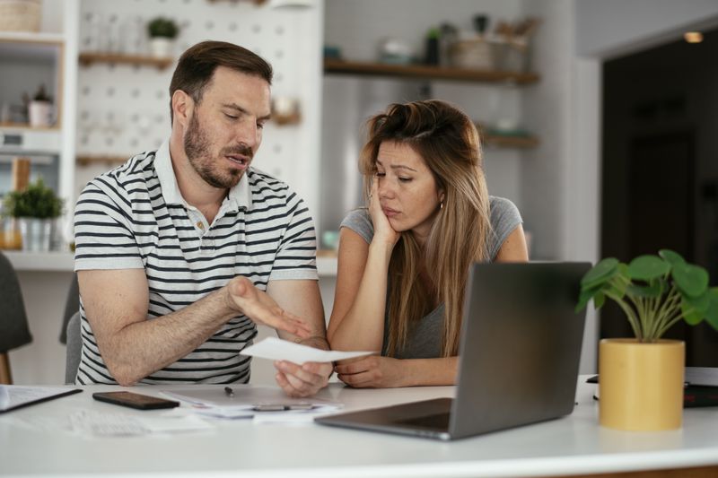 A frustrated couple sitting at home feeling upset about the notice of default they receive from their mortgage lender before pre-foreclosure.