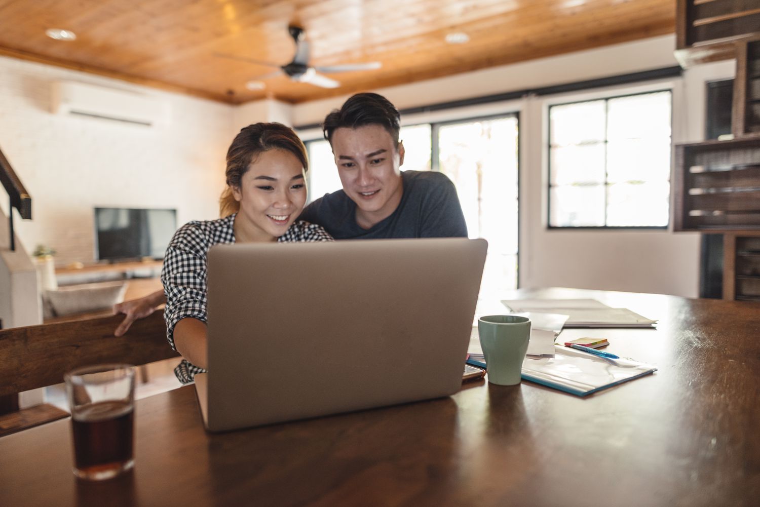 Young couple sitting at dining room table and looking happily together at a laptop