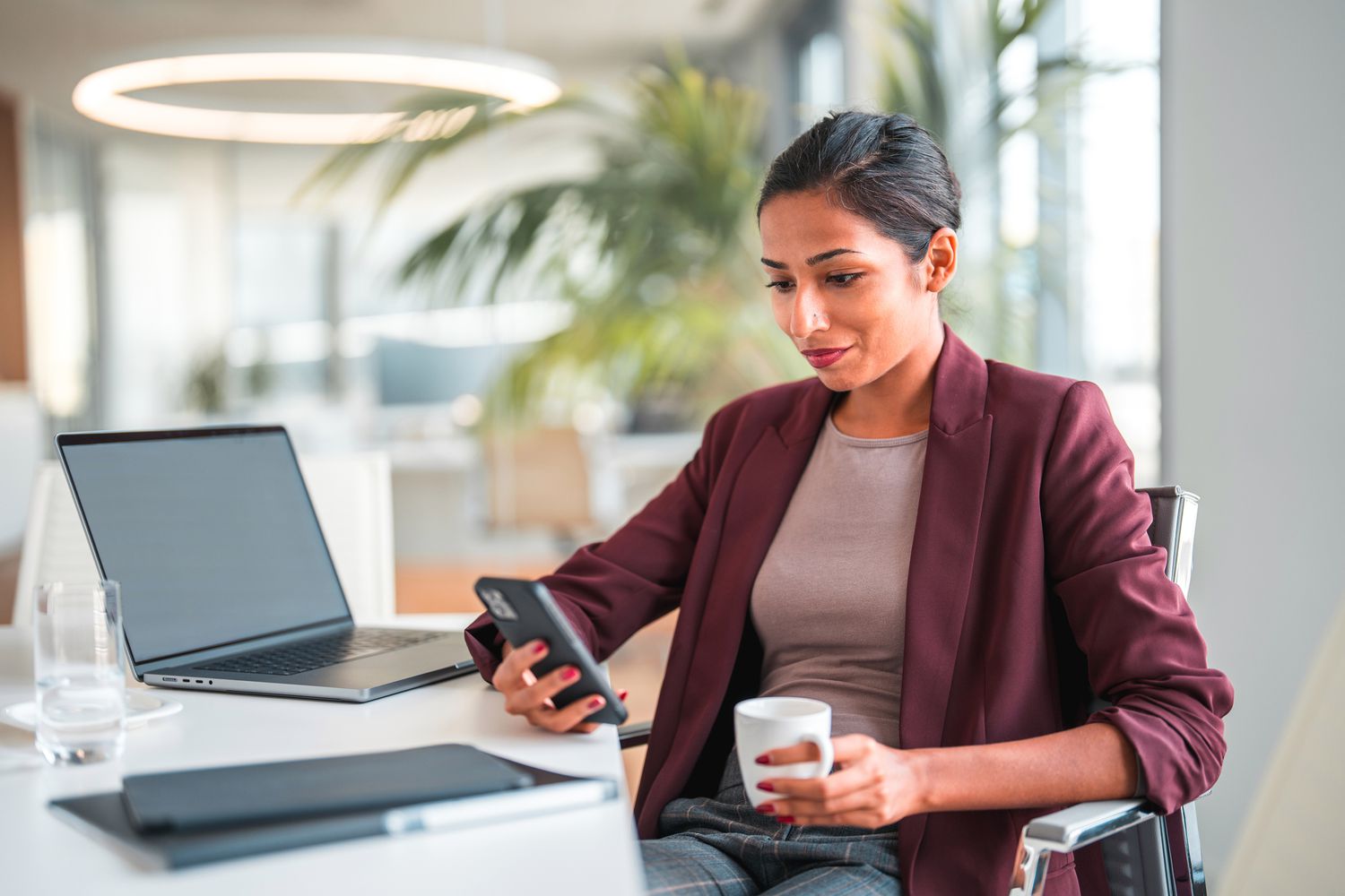 Woman looking at a phone in front of a laptop while sitting in an office. 