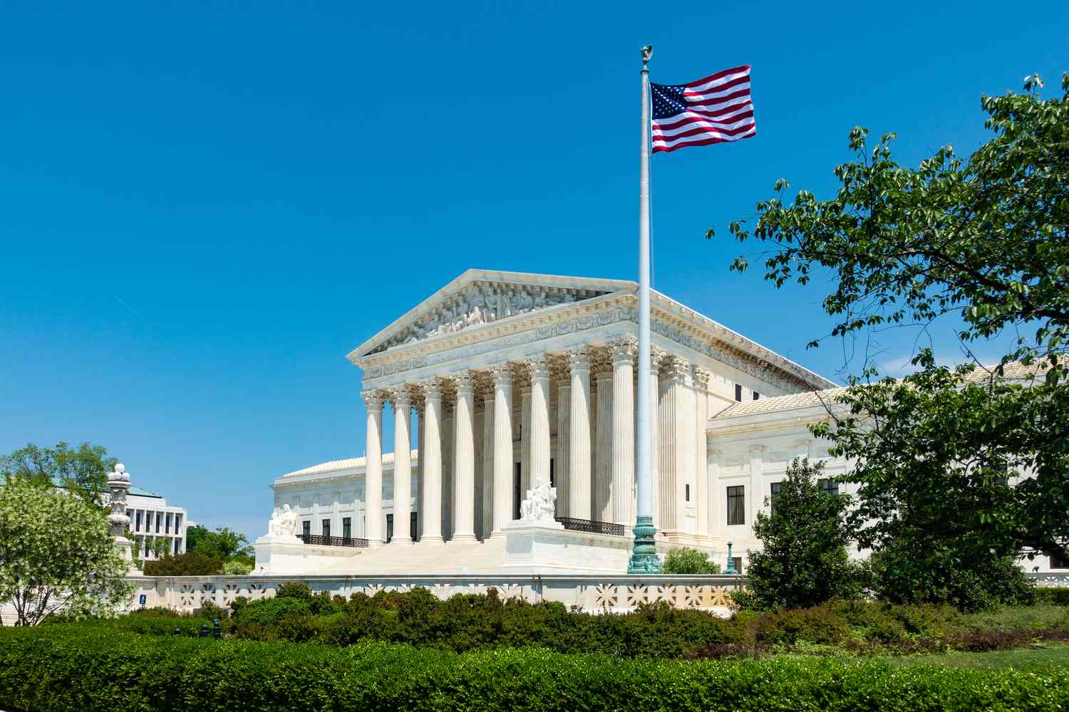 An exterior view of the U.S. Supreme Court building with U.S. flag in the foreground. 