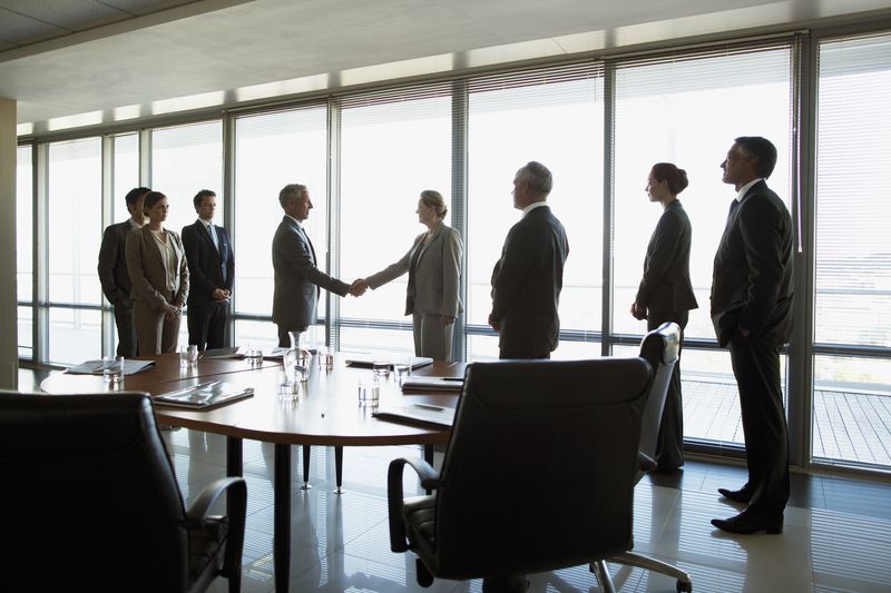 Business workers in an office shaking hands while their coworkers look on