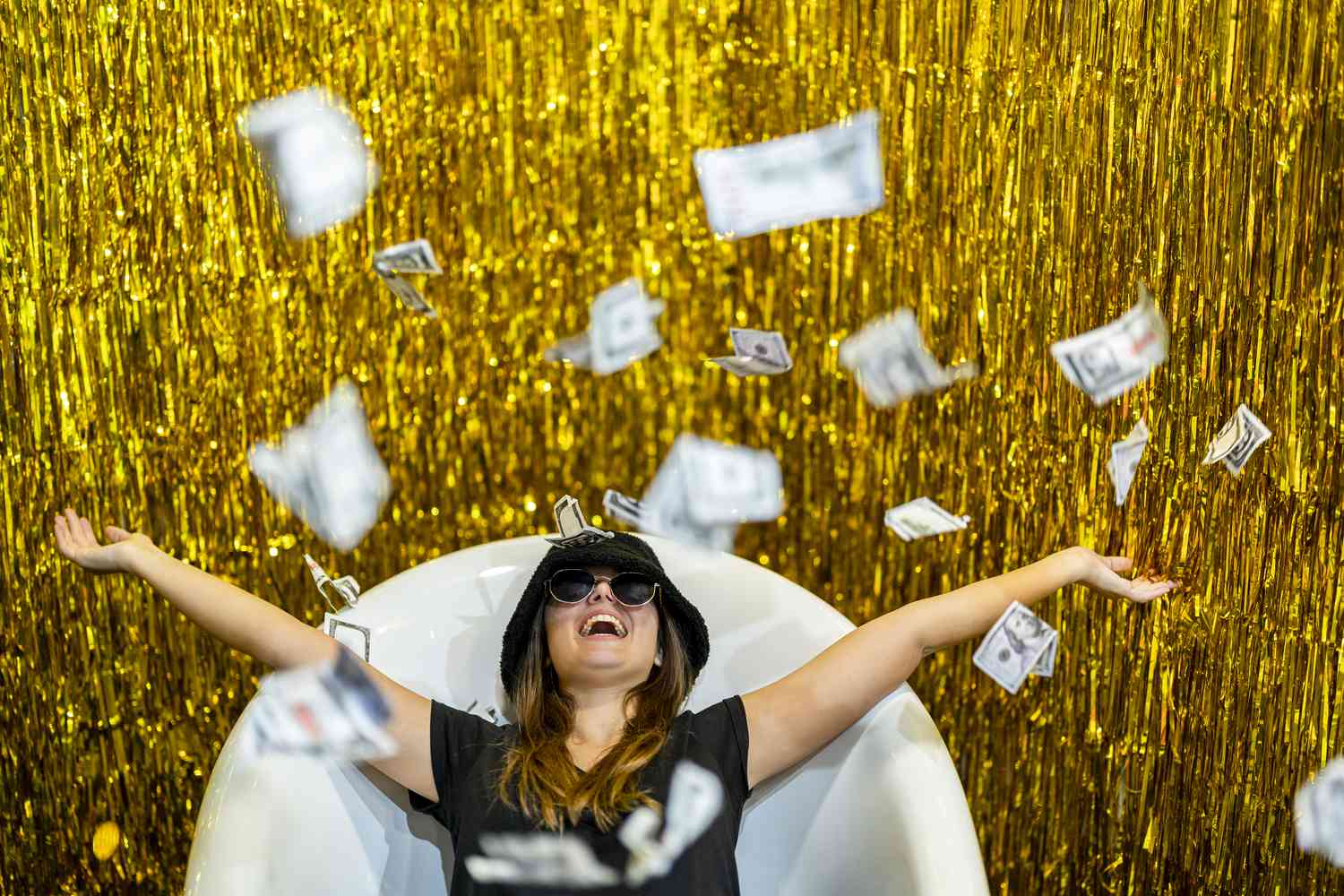Carefree person lying in bathtub with arms outstretched amidst falling Paper Currency