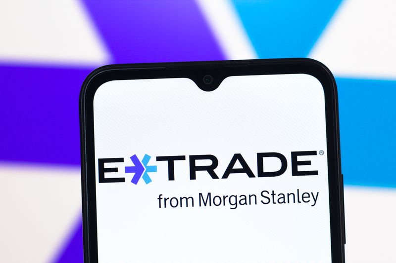 The E*Trade logo is seen on a phone screen, with a larger version of the logo in the background.