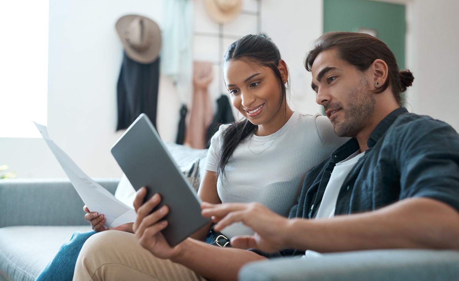 Young couple sitting on their sofa and looking at a mortgage document and a tablet