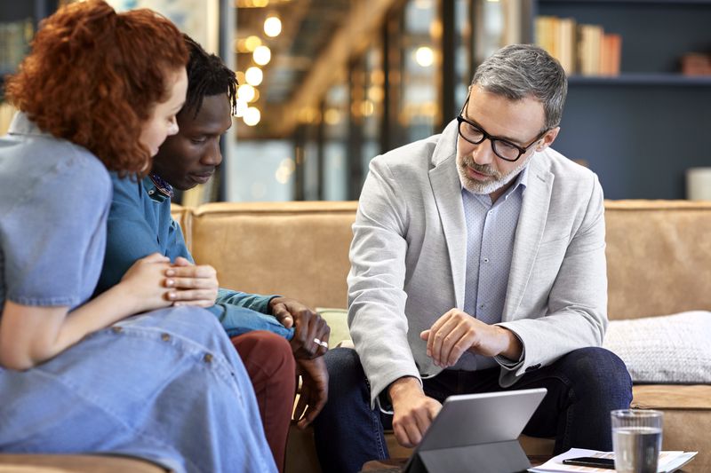 Mature financial advisor planning with young couple in an office setting.